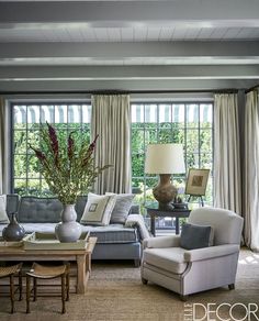 a living room with couches, chairs and lamps in front of two large windows