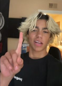 a young man with blonde hair giving the peace sign while wearing a black t - shirt