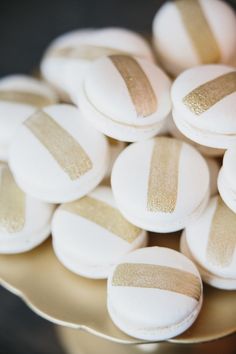 white and gold macaroons are sitting on a golden platter, with one yellow strip across the top