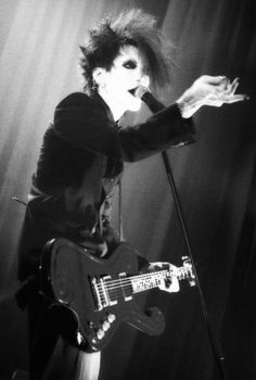 a man with long hair holding a guitar in front of his face and singing into a microphone