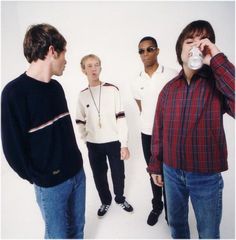 four young men are standing in front of a white wall and one is drinking from a cup