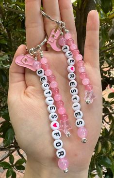 a hand holding two pink and white beaded keychains with words on them