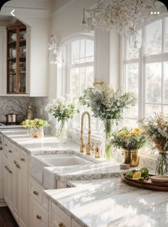 a kitchen with white cabinets and marble counter tops, gold faucets and vases filled with flowers