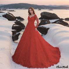 a woman in a long red dress standing on snow covered rocks near the ocean at sunset