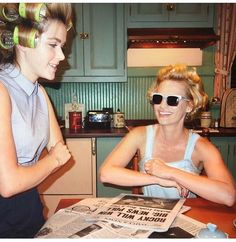 two women sitting at a table with newspapers in front of them and one is wearing sunglasses