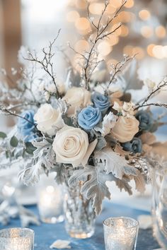 a vase filled with white and blue flowers on top of a table next to candles