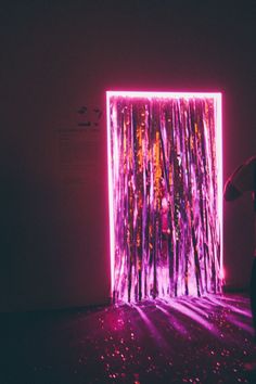 a person standing in front of a purple and pink wall with lights on the floor