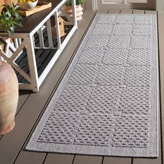 a gray rug sitting on top of a wooden floor next to a potted plant