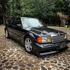 a black car parked on top of a cobblestone road next to trees and bushes