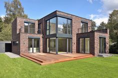 a modern house with wooden deck and glass windows on the front door, surrounded by green grass