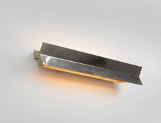 a wall mounted light with a metal blade on it's side and an orange light in the middle