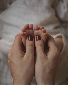 two hands with brown nail polish holding each other's toes in front of the camera