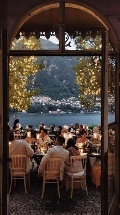 people are sitting at tables in front of an open window with lights on the outside