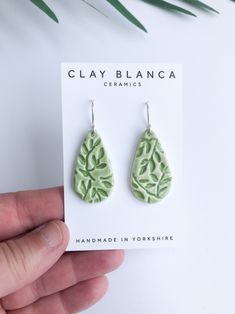 a pair of green earrings with leaves on them sitting in front of a white background