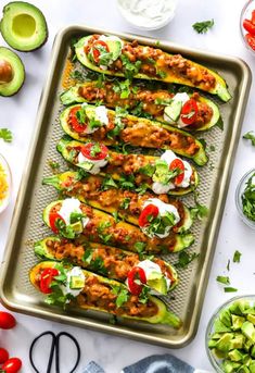 an overhead shot of stuffed avocados on a baking sheet with tomatoes, lettuce and other ingredients