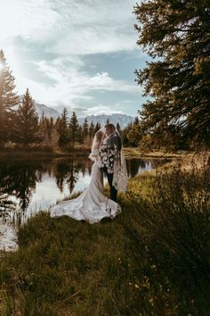 a bride and groom standing in front of a lake