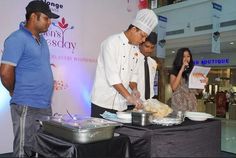 three people standing around a table with food on it and one person holding a piece of paper