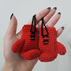 a hand holding two red crocheted mittens with black bows on each one