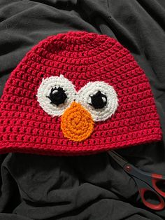 a red crocheted hat with an angry bird face on it and scissors next to it