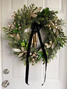 a christmas wreath hanging on the front door with bells and greenery tied around it