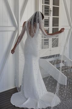 a woman in a white wedding dress with a veil on her head and hands behind her back