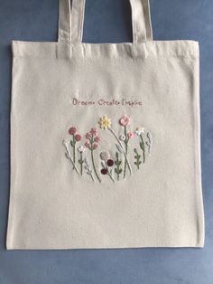 a white bag with flowers embroidered on the front and bottom, sitting on a blue surface