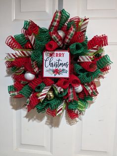 a christmas wreath on the front door with red, green and white ribbons around it