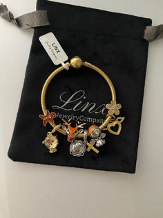 a gold bracelet with charms on it sitting in a black velvet bag next to a tag