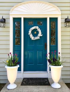 two large white planters sitting in front of a blue door with wreath on it