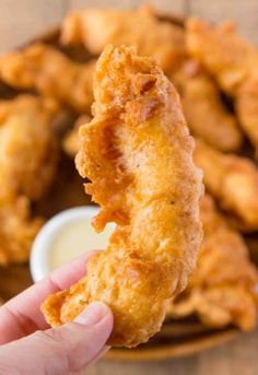 a person holding up a fried chicken nugget in front of some dipping sauce