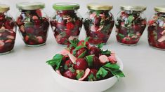 there are many jars filled with cherries and leaves in them on the table next to each other