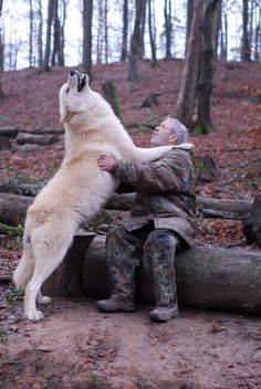 a white dog standing on its hind legs next to a man in camouflage clothing and boots