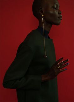 a woman with her hands on her chest wearing gold earrings and a black dress against a red background