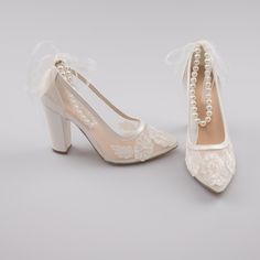 a pair of white shoes with pearls on the heel and lace trimming around the toes