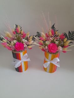 two colorful vases with flowers and leaves on white table top, one is made out of colored pencils