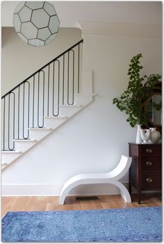 a white bench sitting in front of a stair case next to a blue rug on top of a hard wood floor