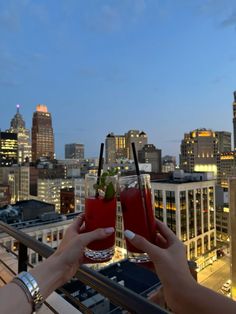 two people holding up drinks in front of a city skyline