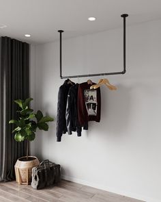 a coat rack with clothes hanging on it next to a plant and purses in front of a window