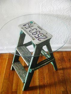 a glass table with a wooden step stool on the bottom and an old metal sign that says peace