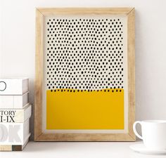 a white coffee cup sitting on top of a table next to a yellow and black painting