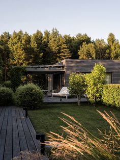 a wooden deck in front of a house surrounded by trees and bushes with a lounge chair on it