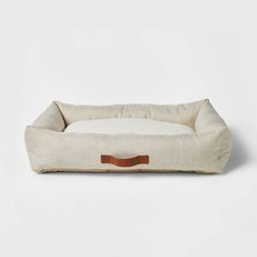 the dog bed is made from natural linen and has a brown leather handle on it