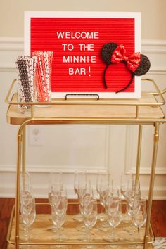 a welcome to the minnie mouse bar with wine glasses and napkins on a gold cart