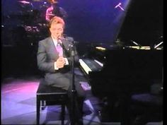 a man sitting at a piano in front of a microphone and singing into a microphone