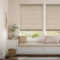 a window seat with pillows on it next to two windows covered in roman blind shades