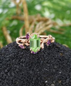 a ring with an amethorate surrounded by purple and green stones sitting on top of a rock