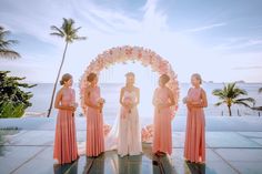 four bridesmaids stand in front of an arch with flowers on it at sunset