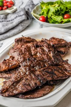 grilled steak on a white plate with salad in the background