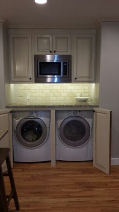 a washer and dryer in a small room with wood flooring, built - in cabinets