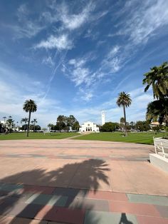 a park with palm trees and a white building in the background, under a partly cloudy blue sky